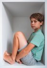 Portrait of brown haired boy sitting in closet, looking at camera. — Stock Photo
