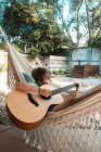 Chico de pelo castaño acostado en una hamaca, tocando la guitarra. - foto de stock
