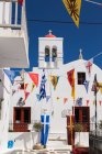 Грецька православна церква та кольорові прапори, що звисають над вузькою алеєю в місті Міконос.. — стокове фото