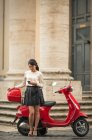 Mujer joven esperando por ciclomotor, Piazza del Popolo, Roma, Italia - foto de stock