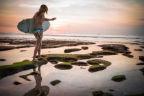 Женщина держит доску для серфинга, идет к морю, Баланган, Бали, Индонезия — стоковое фото