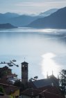 Pueblo frente al mar y montañas lejanas al amanecer, Lago de Como - foto de stock