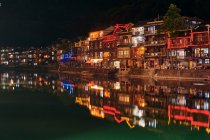 Edificios tradicionales en la orilla del río, iluminados por la noche, Fenghuang - foto de stock