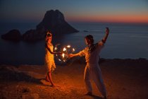 Casal dança com fogo por do sol, Ibiza, Es Vedra rock no backg — Fotografia de Stock