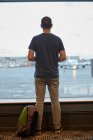 Rückansicht eines Mannes, der am Flughafen aus dem Fenster schaut — Stockfoto