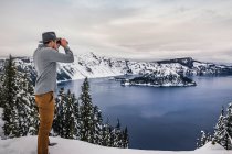 Hombre mirando a través de prismáticos en el lago del cráter en la nieve, Oregon, U - foto de stock