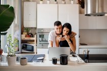Young lesbian couple standing in kitchen, using laptop. — Stock Photo