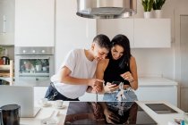 Молодая лесбийская пара, стоящая на кухне, глядя на мобильный телефон — стоковое фото