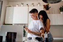 Junges lesbisches Paar steht in Küche und schaut auf Handy — Stockfoto