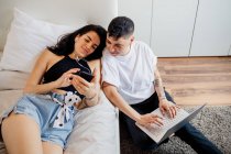 Jovem casal lésbico em um quarto, usando telefone celular e laptop — Fotografia de Stock