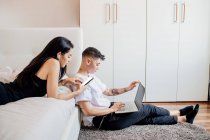 Young lesbian couple in a bedroom, using mobile phone and laptop — Stock Photo