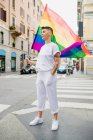 Giovane donna lesbica in piedi su una strada, sventolando bandiera arcobaleno. — Foto stock