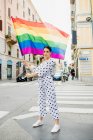 Jovem lésbica de pé em uma rua, acenando bandeira do arco-íris. — Fotografia de Stock