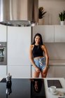 Portrait of young woman with long brown hair, wearing hot pants, standing in kitchen — Stock Photo