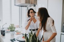 Two women with brown hair standing in a kitchen, eating sushi. — Stock Photo