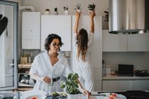 Дві усміхнені жінки з коричневим волоссям стоять на кухні, готуючи їжу . — стокове фото