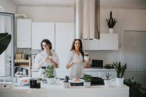 Две улыбающиеся женщины с каштановыми волосами стоят на кухне и готовят еду.. — стоковое фото