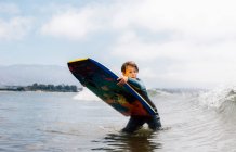 Retrato de un niño joven con traje de neopreno en el océano, sosteniendo bodyboard, esperando ola, Santa Barbara, California, EE.UU.. - foto de stock
