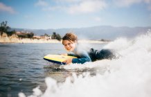 Portrait of young boy wearing wet suit, lying on surfboard, riding wave, Santa Barbara, California, USA. — Stock Photo