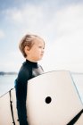 Retrato de un joven con traje de neopreno, llevando tabla de surf al océano, Santa Barbara, California, EE.UU.. - foto de stock