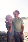 Retrato de dois meninos sorridentes, em pé na praia, braço em torno do ombro, olhando para a câmera, Santa Barbara, Califórnia, EUA. — Fotografia de Stock