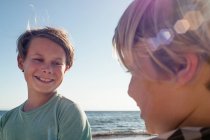 Retrato de la cabeza y los hombros de dos chicos sonrientes junto al océano. - foto de stock