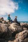 Two boys sitting on rocks by the ocean near Carmel, California, USA. — Stock Photo