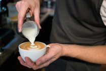 Close up of barista pouring milk foam onto cappuccino cup. — Stock Photo