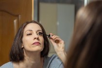 Femme debout devant le miroir, appliquant le maquillage — Photo de stock