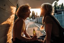 Junges weibliches Paar trinkt ein Bier im Heck seines Lieferwagens — Stockfoto