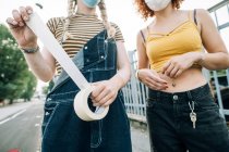 Mulheres jovens usando máscaras, segurando rolo de fita — Fotografia de Stock