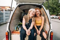 Жіноча пара сміється, сидячи позаду фургона — стокове фото