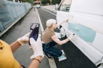 Frau fotografiert Freundin beim Malen von Lieferwagen — Stockfoto