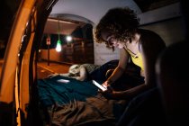 Junge Frau schaut aufs Handy, während ihr Partner im hinteren Teil des Lieferwagens schläft — Stockfoto