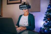 Femme utilisant casque de réalité virtuelle et ordinateur portable — Photo de stock