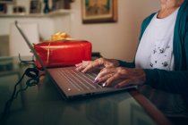 Mulher usando laptop com presente de Natal ao lado dela — Fotografia de Stock
