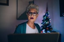 Femme utilisant un ordinateur portable la nuit, arbre de Noël en arrière-plan — Photo de stock