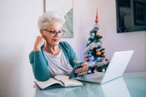 Frau arbeitet zu Hause, Weihnachtsbaum im Hintergrund — Stockfoto