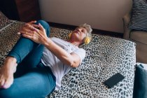 Женщина отдыхает в постели, слушает наушники и растягивается — стоковое фото