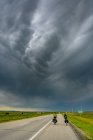 Ciclistas en carretera bajo un cielo tormentoso, Ontario, Canadá - foto de stock