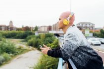 Mujer en puente, escuchando música en auriculares - foto de stock