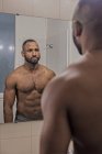 Mann mit nacktem Oberkörper sieht sich im Badezimmerspiegel an — Stockfoto