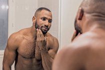 Чоловік дивиться у дзеркало, торкаючись бороди — стокове фото