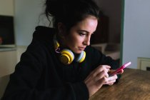 Junge Frau mit Kopfhörern und Blick auf ihr Handy — Stockfoto
