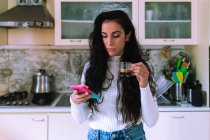 Молодая женщина пьет кофе и смотрит в телефон — стоковое фото