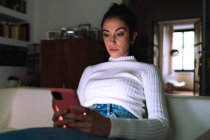 Junge Frau schaut zu Hause auf ihr Handy — Stockfoto