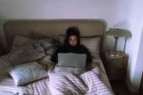 Mujer joven trabajando en el ordenador portátil en la cama - foto de stock