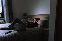 Молода жінка використовує мобільний телефон у ліжку — стокове фото