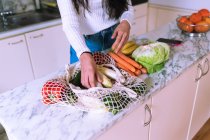 Mujer desempacar verduras en la cocina - foto de stock