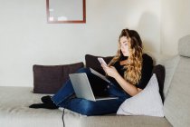 Jovem mulher usando smartphone e laptop em casa — Fotografia de Stock